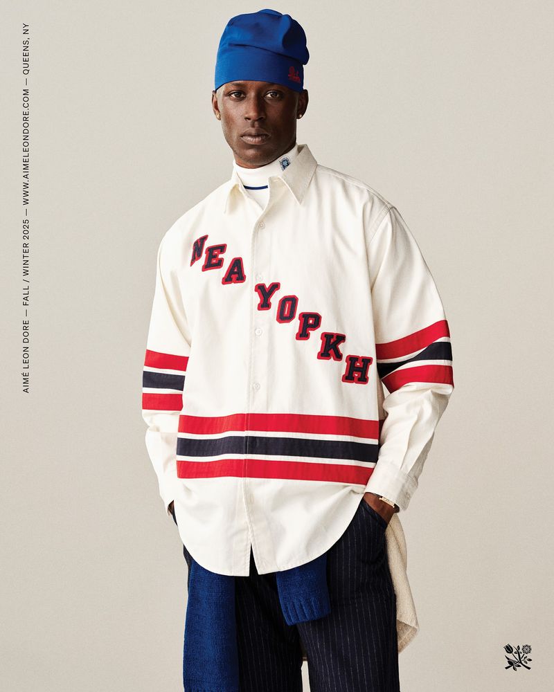 Fashion shot of a Black male model in a white shirt with red and black stripes, and a blue beanie, posing in a photo studio.