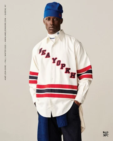 Fashion shot of a Black male model in a white shirt with red and black stripes, and a blue beanie, posing in a photo studio.