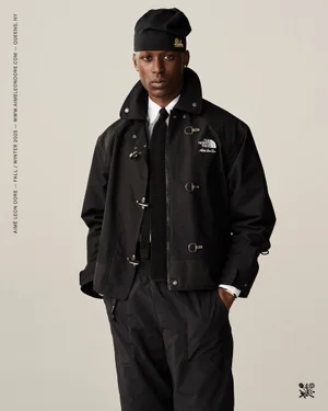 Model in black jacket, tie, and beanie against a plain light background for Aimé Leon Dore F/W 2025 lookbook.