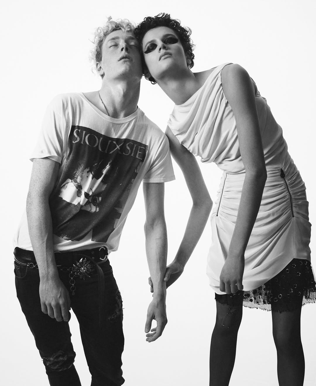 Monochrome fashion portrait of a pair of models posing together in a photo studio wearing white dress and graphic tee.