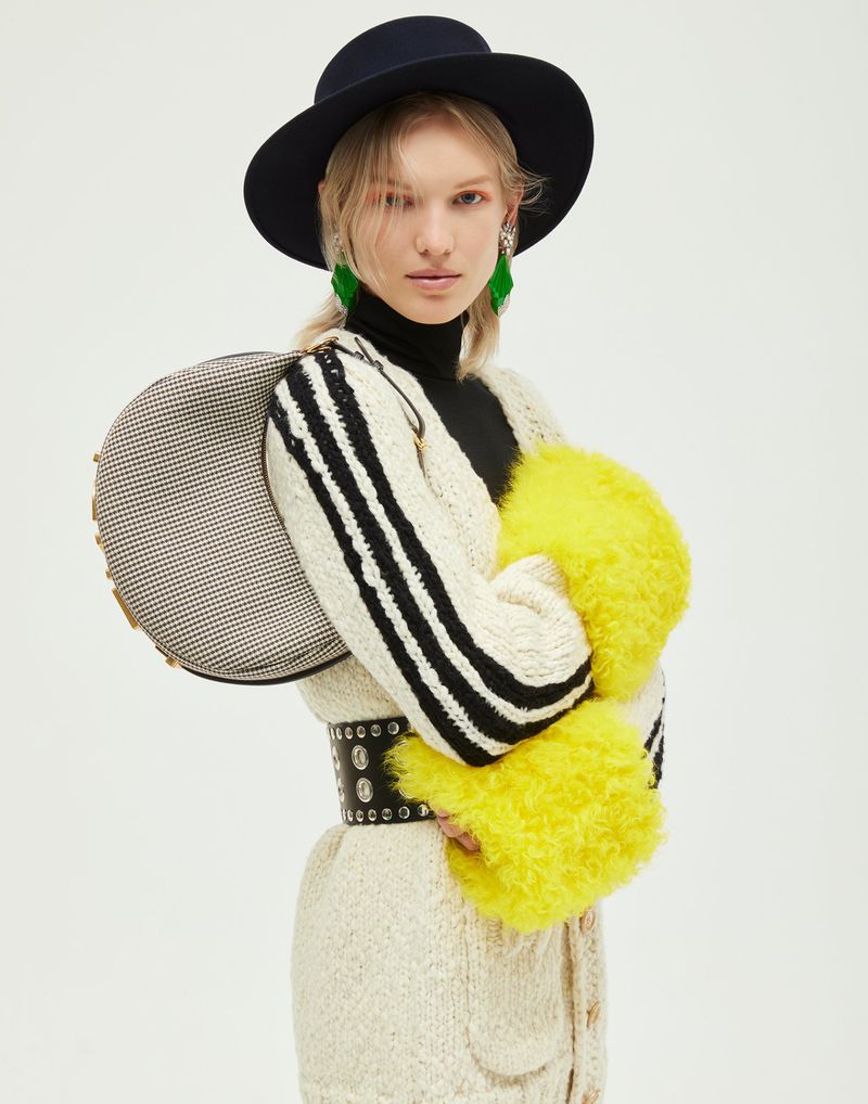 Fashion portrait of a blonde woman in a black hat, sweater, and black skirt with a grey and black purse and yellow fur accents.