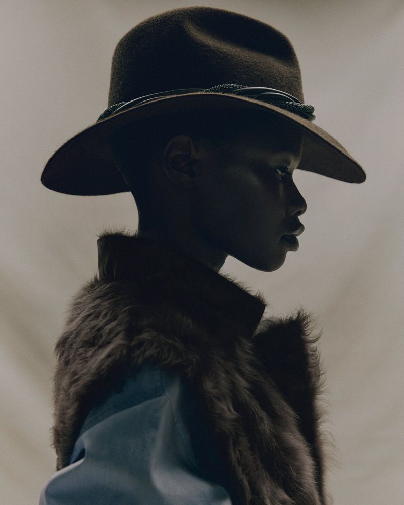 Portrait of a Black woman with a brown hat and fur collar, featuring a side view and a light grey background, creating a stylish image.