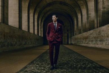 Model Juhyung Kang walks down a vaulted stone corridor wearing a burgundy velvet double-breasted suit and tie.