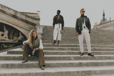 Four models pose on monumental stone outdoor steps featuring classical architecture under an overcast sky.