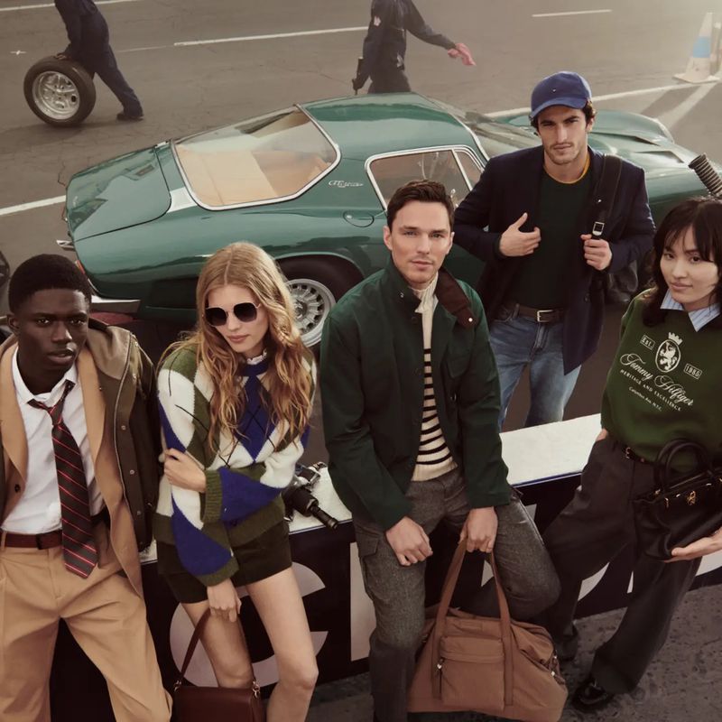 Group of fashion models pose with a vintage sports car on an outdoor course, wearing preppy clothing from Tommy Hilfiger.