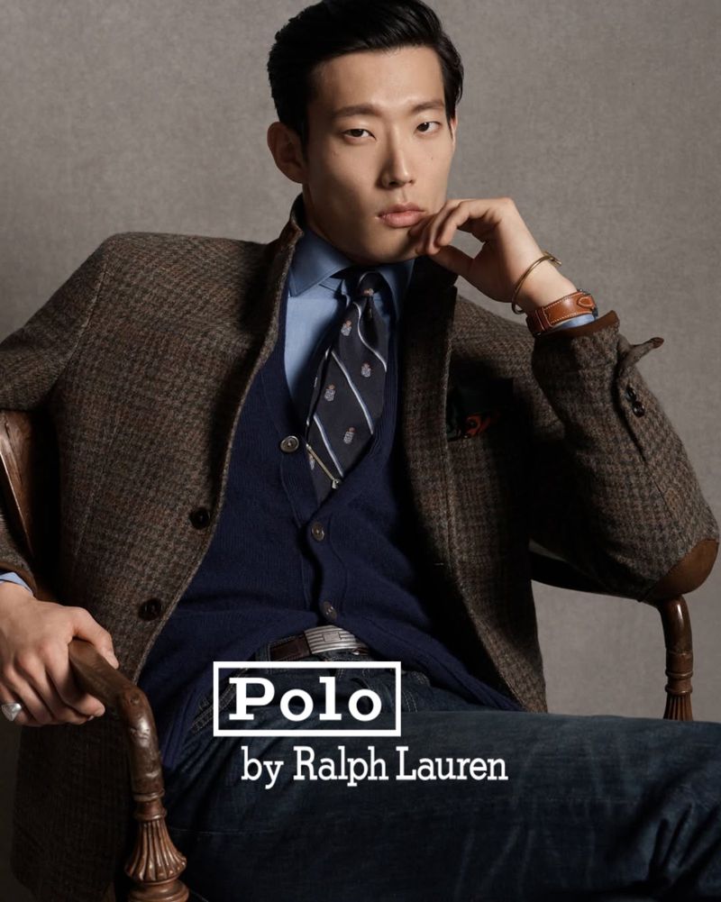Model Juhyung Kang seated in a wooden armchair wearing a brown tweed blazer and navy tie for Polo Ralph Lauren.