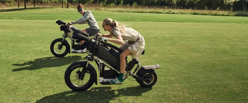 Two people ride electric golf scooters on a lush green golf course on a sunny day, carrying golf club bags. Golf and leisure.