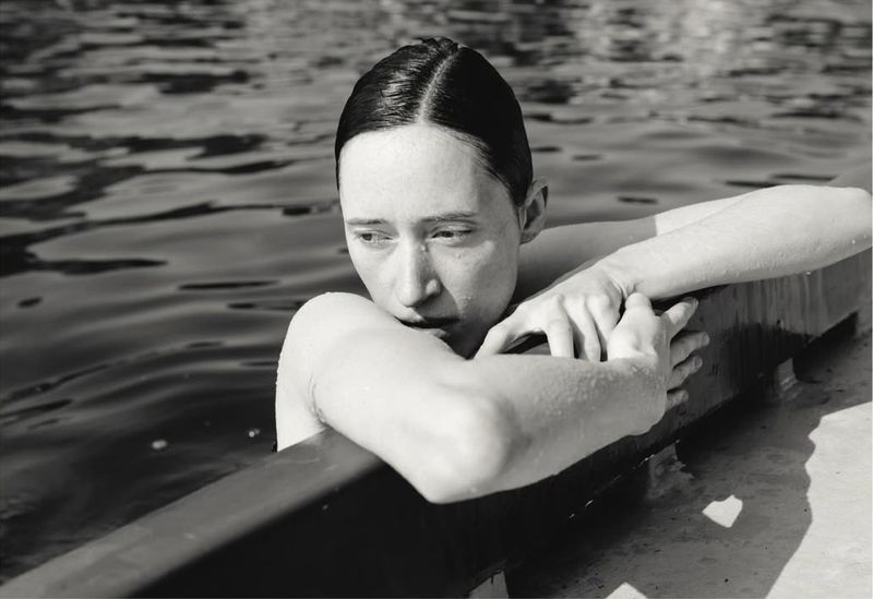 Monochrome portrait of a woman in water, resting her arms on a ledge, creating a serene and intimate atmosphere in natural light.