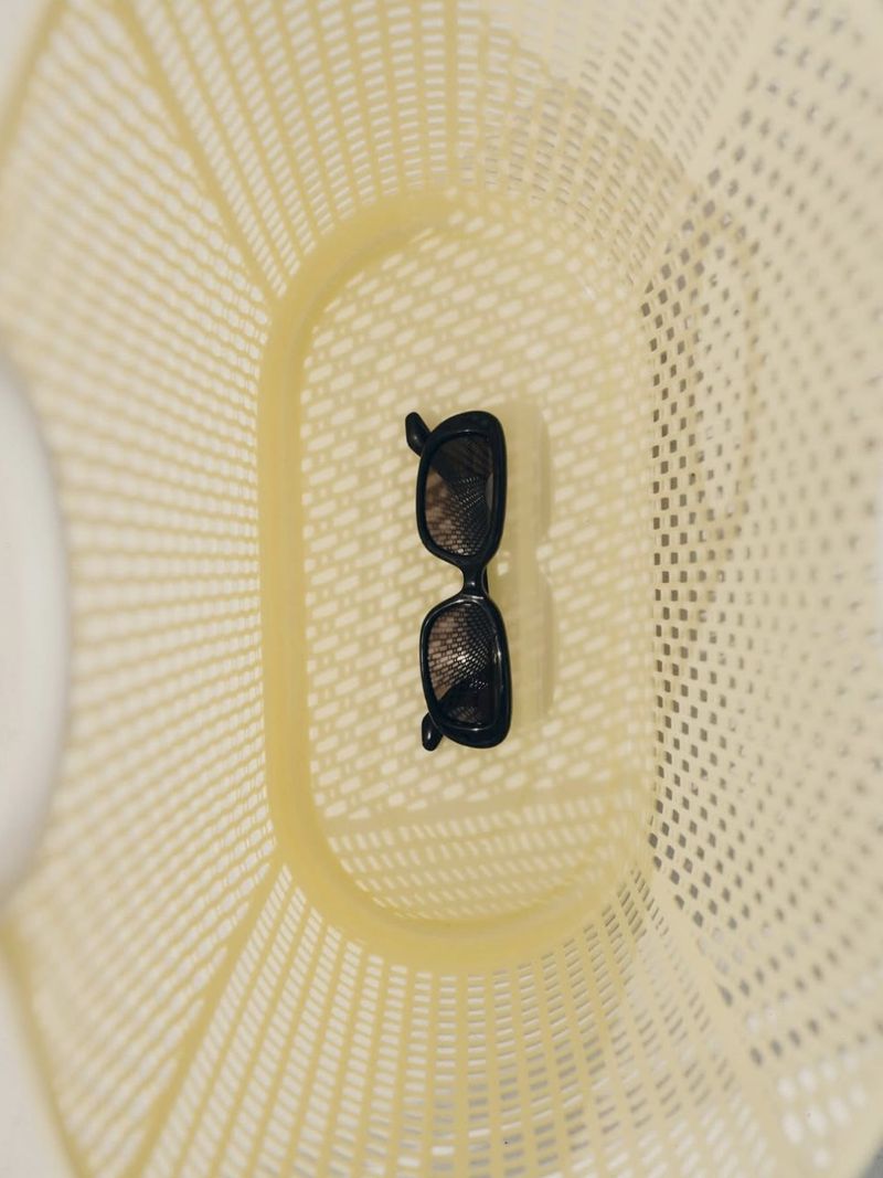 Sunglasses rest inside a woven tan net-like bag. A close-up of the glasses and net bag fills the frame, casting soft shadows.