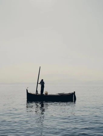 Silhouette of Helena Severin standing on a small wooden boat on calm misty open water for Vince by Charlotte Lapalus.
