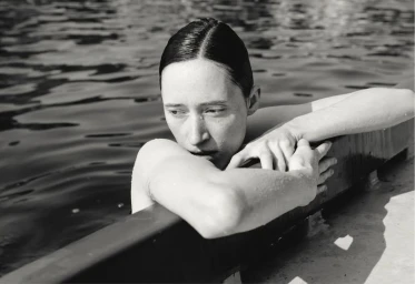 Black and white photo of model Helena Severin resting her arms along the edge of an outdoor pool.
