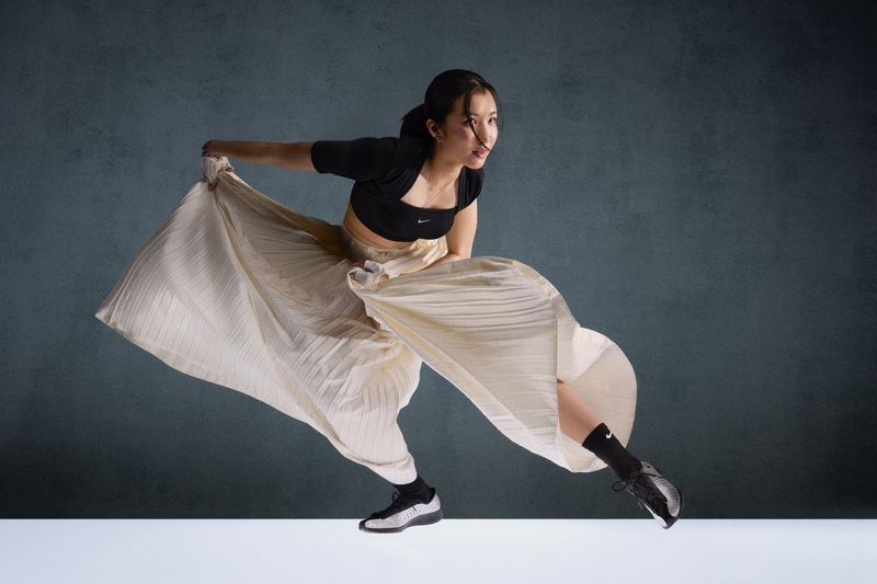 Young woman in motion, wearing a crop top, skirt and sneakers, strikes a dynamic pose against a textured background, showcasing athleticism.