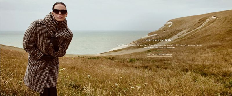 A woman in sunglasses and a checkered coat stands in a grassy field with the sea and cliffs in the background. Fashion outdoor shot.