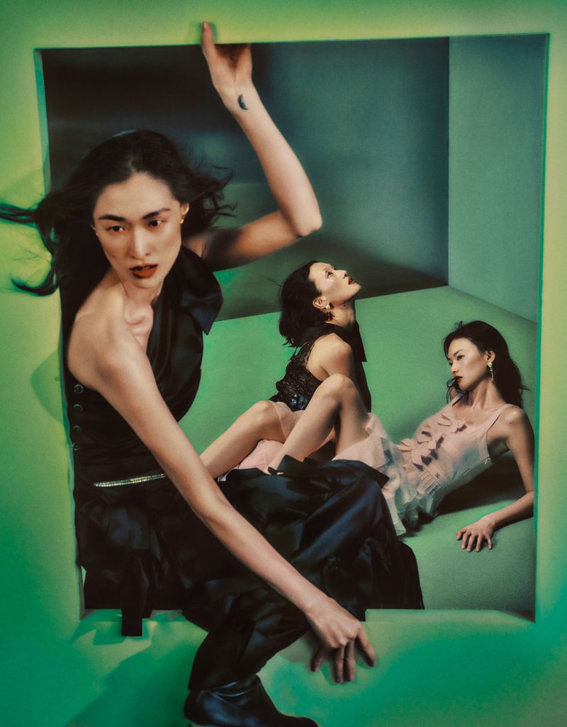 Three Asian women in fashionable clothing pose in a neon green box in a studio. One woman is wearing black and the others, light dresses.