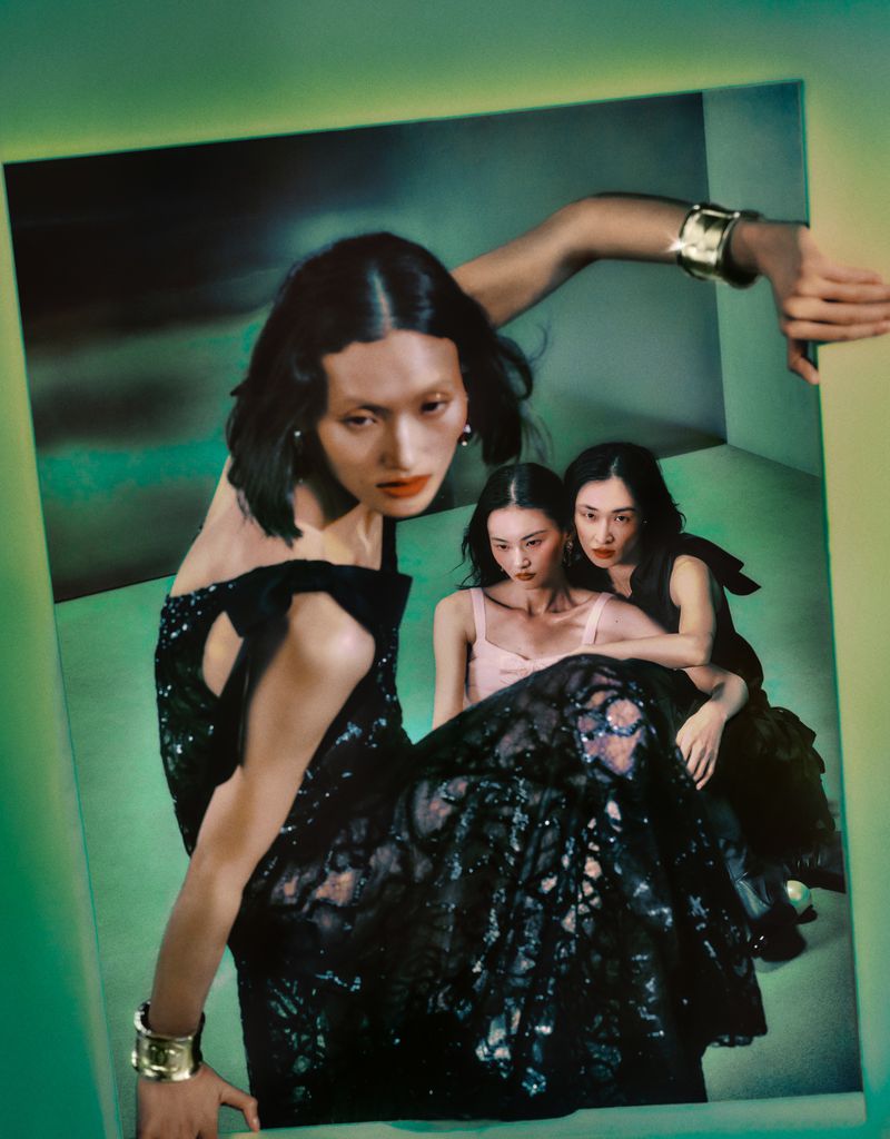 Three Asian women in a retro-style fashion shot; one woman in foreground wearing a black gown and gold cuff bracelet. Fashion editorial.