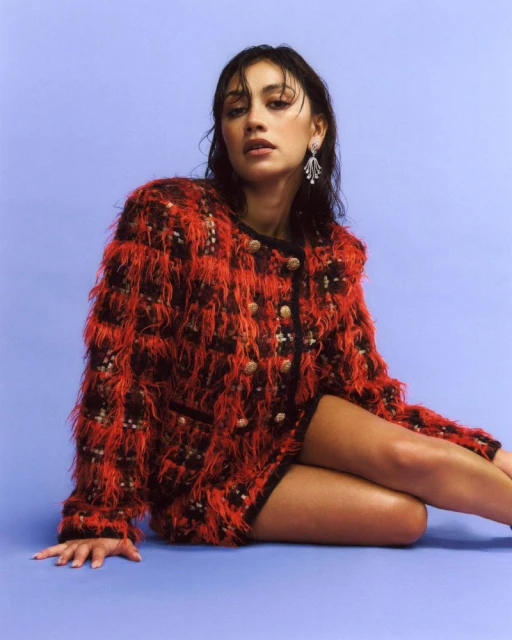 Woman in a red tweed jacket with pearl buttons sits against a lilac background, showcasing fashion, style, and portrait photography.