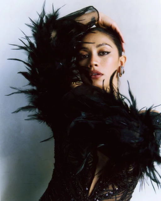 Glamorous portrait of a woman with black feathered boa. She is wearing jewelry and posing with her hand on her head.