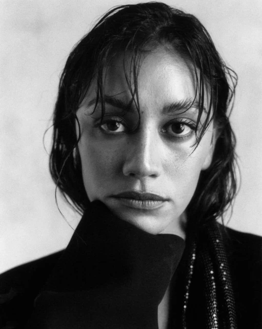 Monochrome portrait of a young woman with wet dark hair, looking at the camera while resting her chin on her gloved hand.