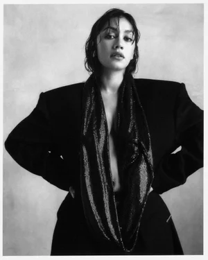 Luciane Buchanan posing in an oversized black blazer with a draped shimmering scarf in a black and white studio portrait.