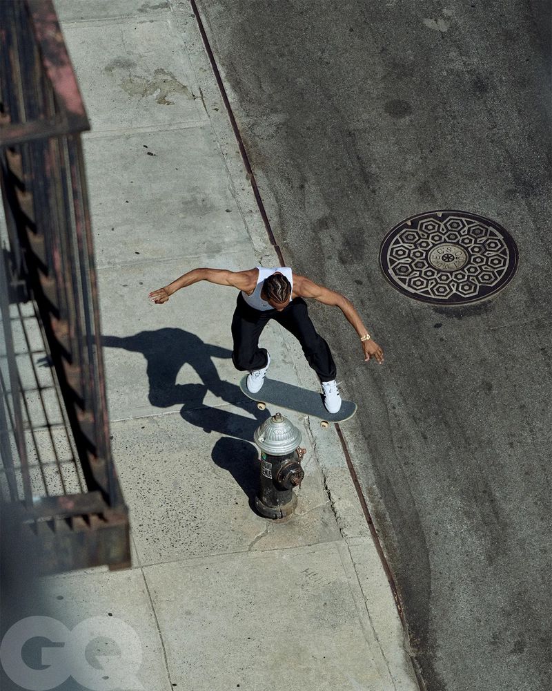 Overhead shot of adult male skateboarding on sidewalk in city street near fire hydrant, showing urban environment and GQ logo.