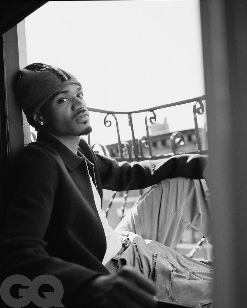 Black and white portrait of a stylish adult male with a beanie, in an urban setting, gazing into the distance, providing a sense of depth and mood.