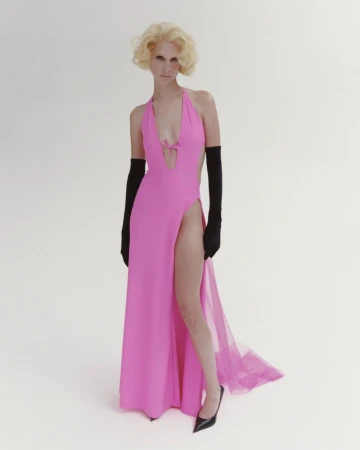 Fashionable woman posing in a pink halter dress with a thigh-high slit, paired with elegant black gloves and stiletto heels, studio setting.