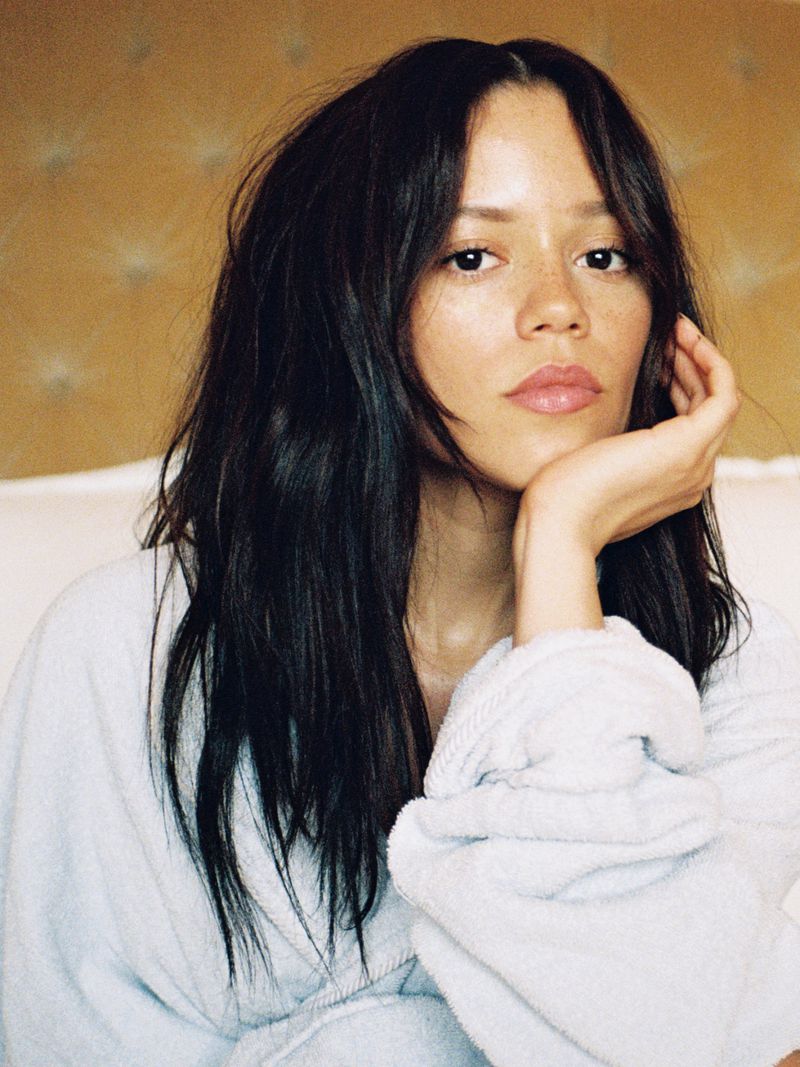 Portrait of a woman with long dark hair wearing a light-blue robe, posing indoors with her hand to her face. Beauty and fashion.