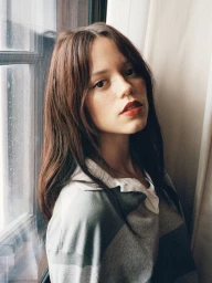 Jenna Ortega standing near a window wearing a striped polo shirt for a Vogue editorial feature