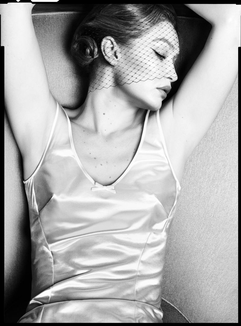 Black and white portrait of a woman with a veil lying down in a satin dress, eyes closed, arms raised, showcasing an elegant, vintage style.