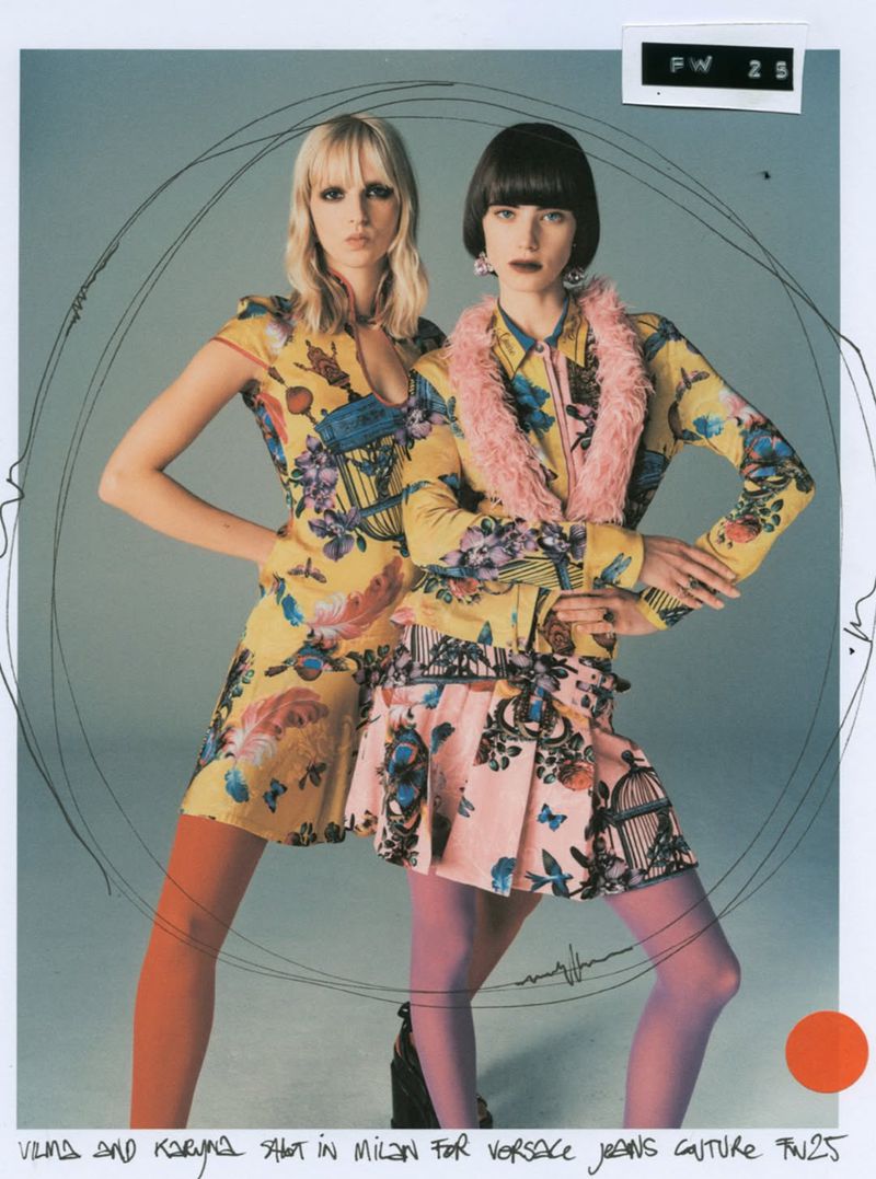 Two fashion models pose in a studio wearing outfits with floral and birdcage patterns, one with a pink faux fur collar.