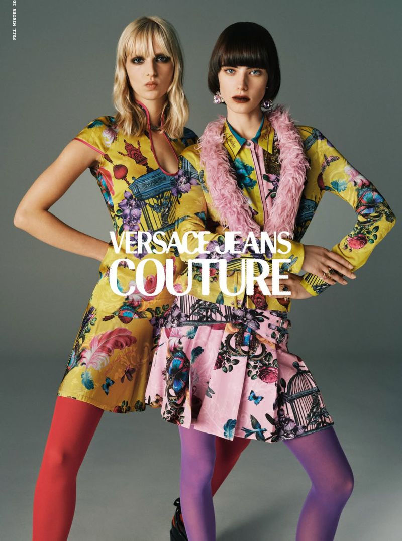 Two young fashion models in Versace Jeans Couture collection, posing in brightly colored floral dresses and matching tights, studio shot.