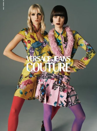 Two young fashion models in Versace Jeans Couture collection, posing in brightly colored floral dresses and matching tights, studio shot.