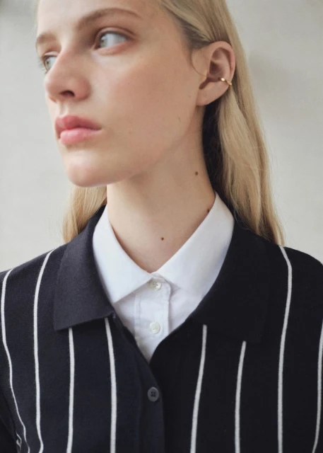 Close-up shot of a fair-skinned woman with blonde hair wearing an open black and white striped shirt over a white collared shirt.