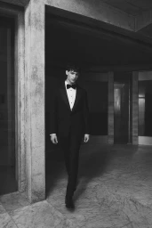 Model Jonathan Azar in a black tuxedo and bow tie standing in an architectural interior for Calibre 2025 Campaign