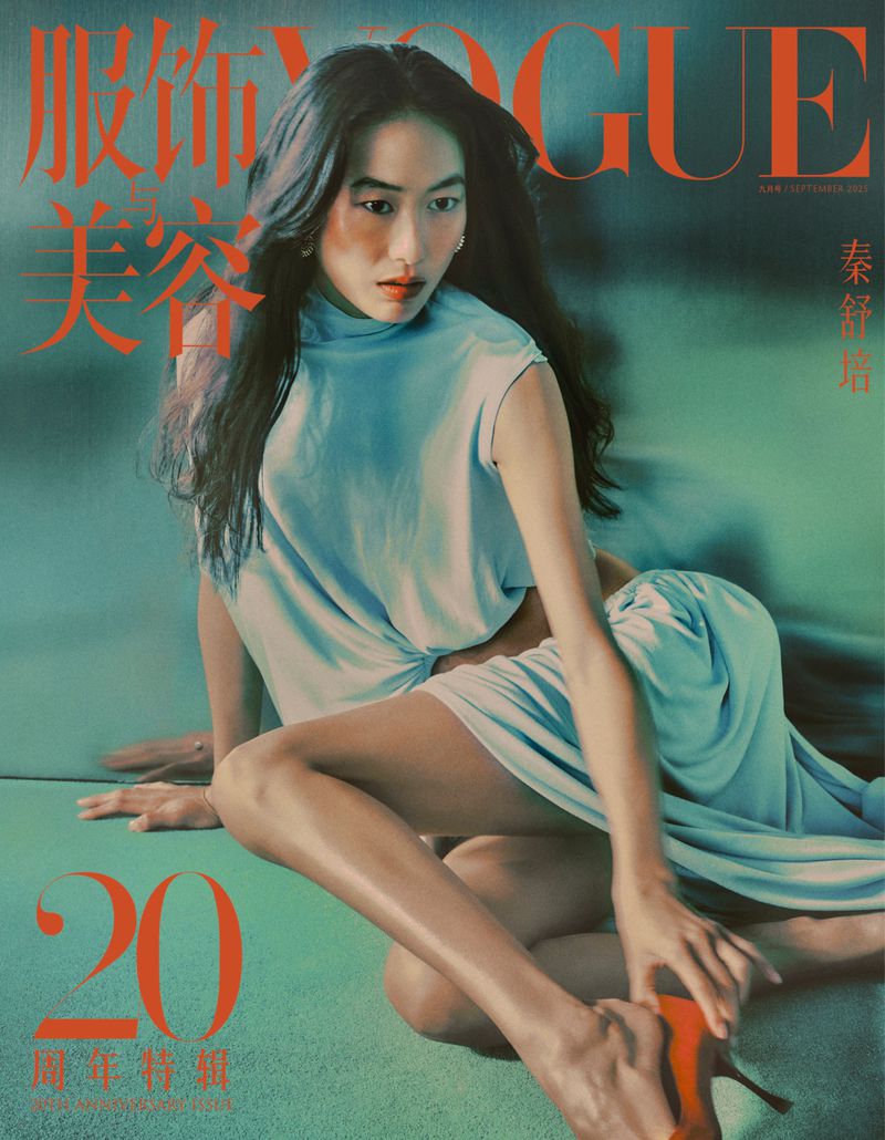 Vogue cover featuring a model in a light blue dress, seated against a muted green backdrop, showcasing fashion and beauty elements.