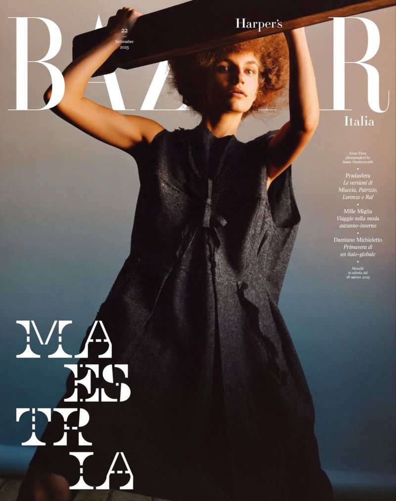Fashion magazine cover with a model posing with a wooden plank, wearing a dark dress against a gradient background. Harper's Bazaar Italia.