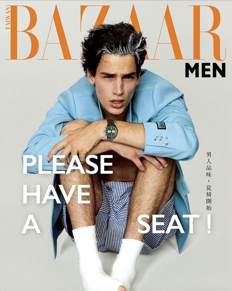 Bazaar Men cover features a model in a blue blazer and striped shorts seated against a light backdrop, showcasing fashion and editorial style.