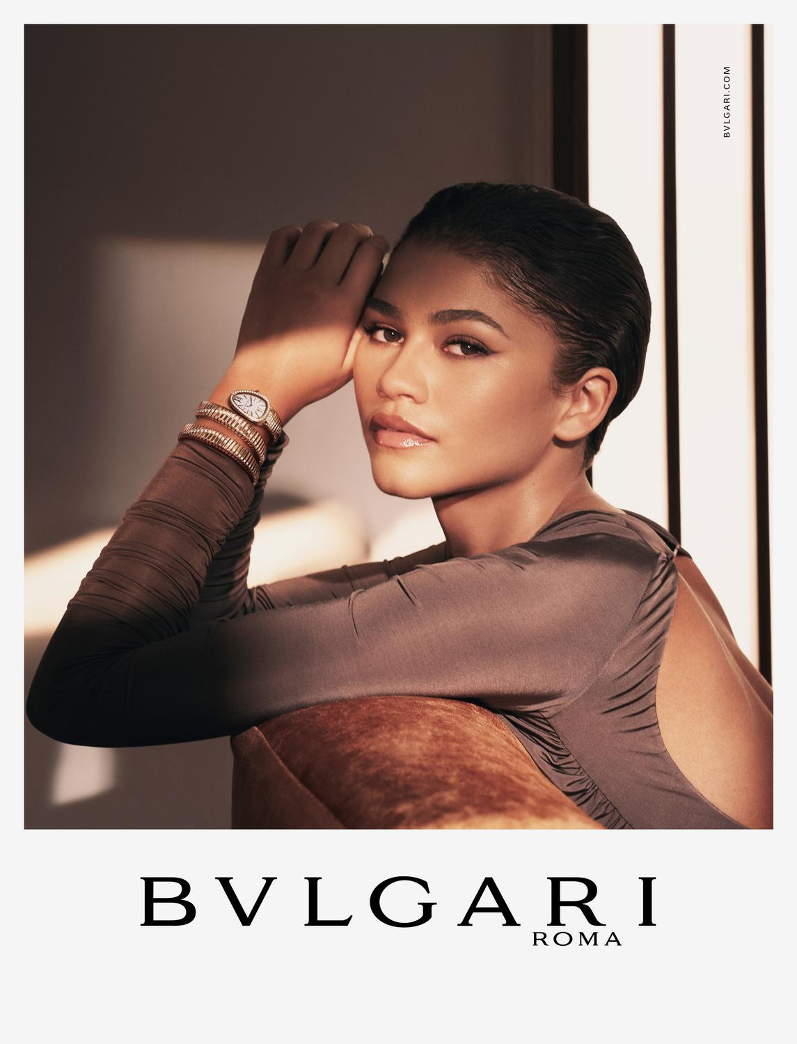 Close-up studio shot of Zendaya wearing Bulgari watch, bracelets, and a sleek taupe dress, set against a soft, neutral backdrop.