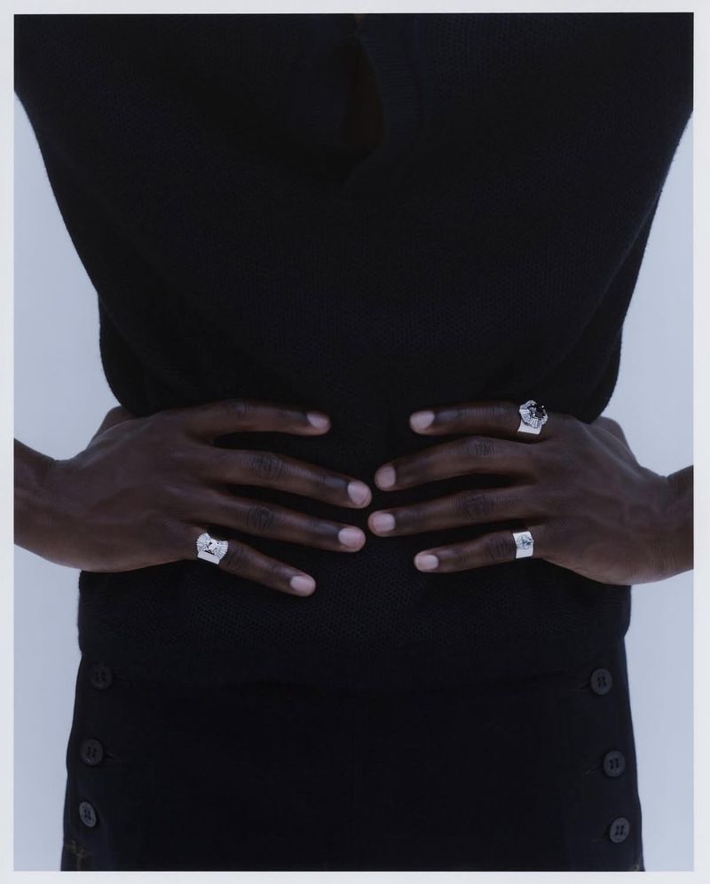 Person wearing three silver rings and a black shirt, holding their waist in a studio setting with a light grey background.