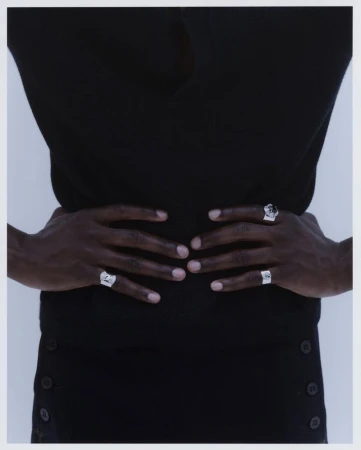 Close-up of model Mani Adjaye with hands resting on waist showcasing ornate silver rings against a pale studio backdrop.