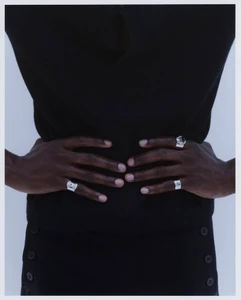 Close-up of model Mani Adjaye with hands resting on waist showcasing ornate silver rings against a pale studio backdrop.