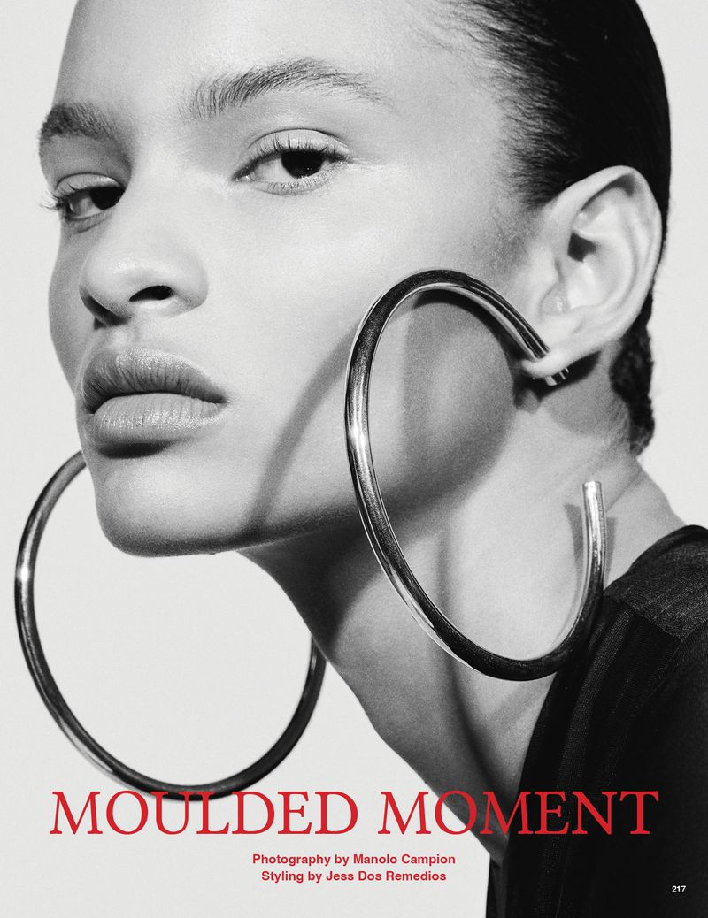 Close-up of a model wearing hoop earrings. The shot is monochrome, highlighting the earring's design and the model's facial features.
