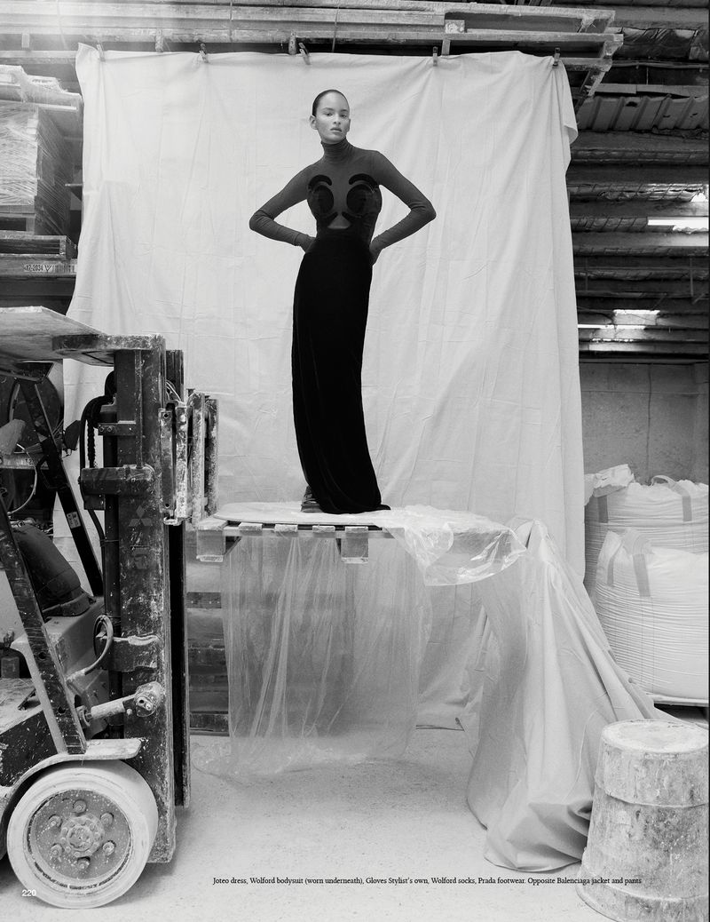 Fashion shot of a woman in a black dress standing on a pallet in a warehouse setting, next to a forklift and under a white sheet.