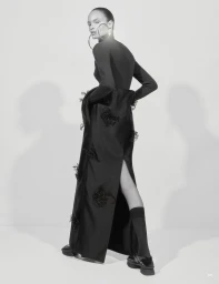 Model Ana Portela wearing a long black embellished gown, oversized hoop earrings, and platform shoes against a studio backdrop.