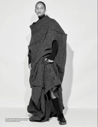 Model Ana Portela wearing an oversized sculptural grey wool coat and black loafers against a light studio backdrop.