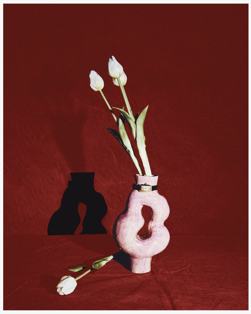 Still life of white tulips in a light pink vase against a deep red background with dark shadow; one tulip rests on its side.