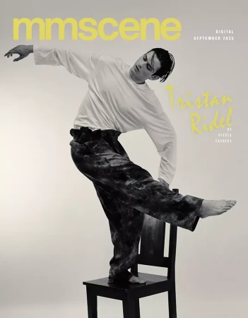 Fashion magazine cover featuring a male model in a white top and velvet pants, balancing on a black chair against a neutral background.