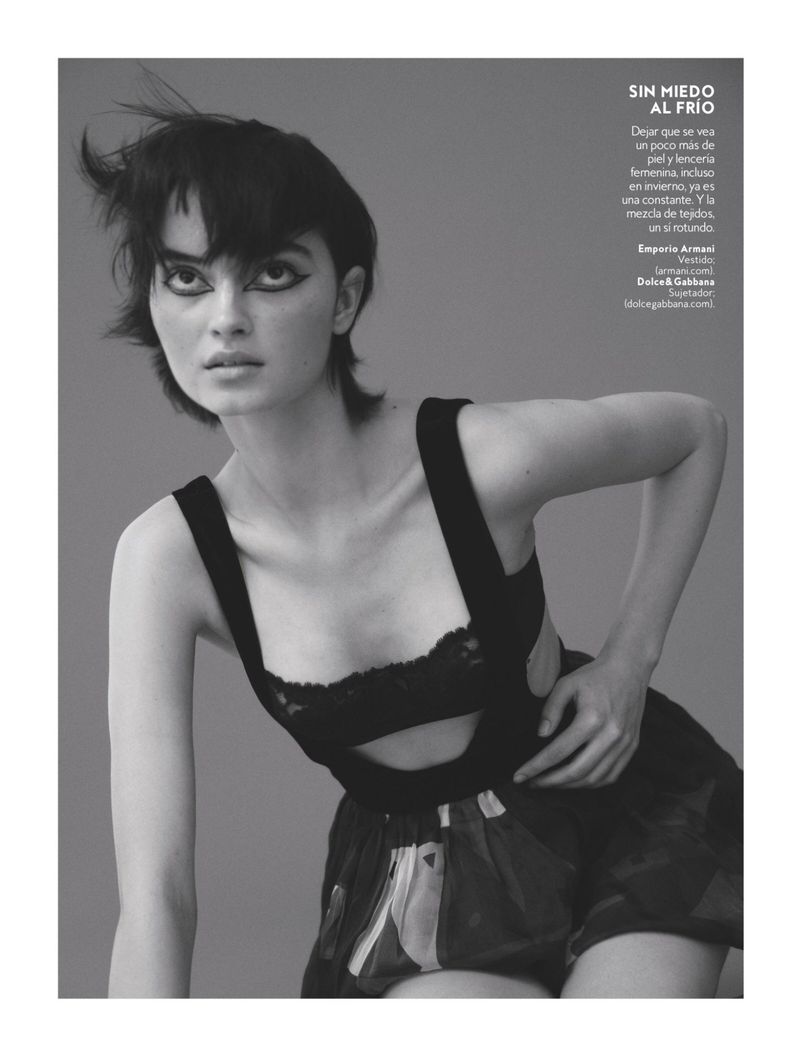 Black-and-white fashion photo of a woman with dark hair and heavy eyeliner, wearing a black lingerie top and printed shorts.
