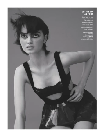 Black-and-white fashion photo of a woman with dark hair and heavy eyeliner, wearing a black lingerie top and printed shorts.
