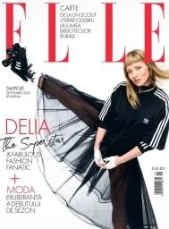 Singer Delia performing a high kick wearing black roller skates, an Adidas top, and a black sheer tulle skirt against a white backdrop.